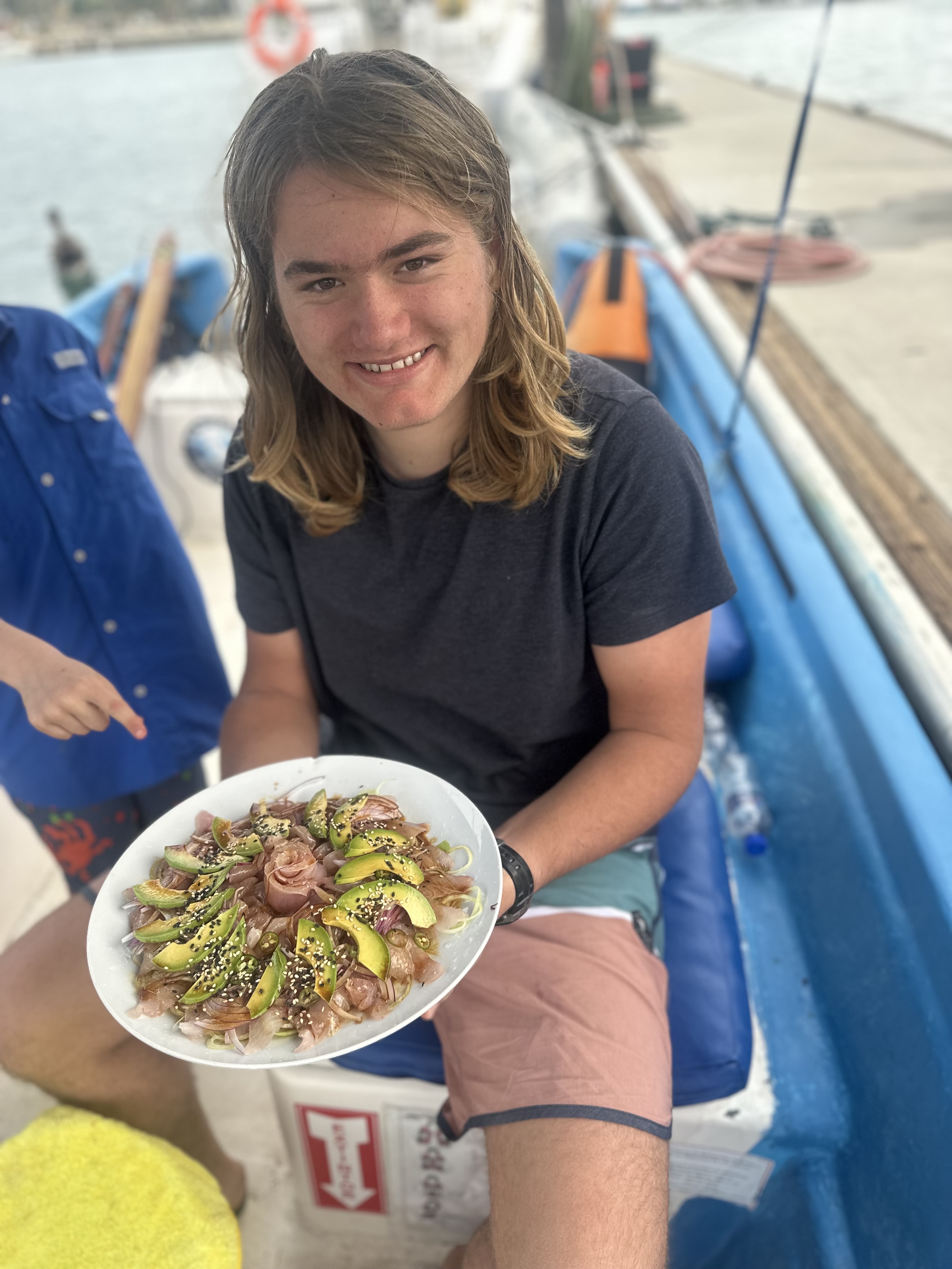 18 year old boy with shoulder length blond hair holding a plate of sashimi from a fish he caught
